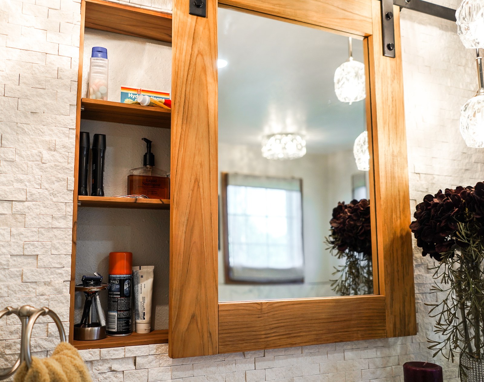 A bathroom with a wood sliding mirror cabinet on a white stacked stone wall