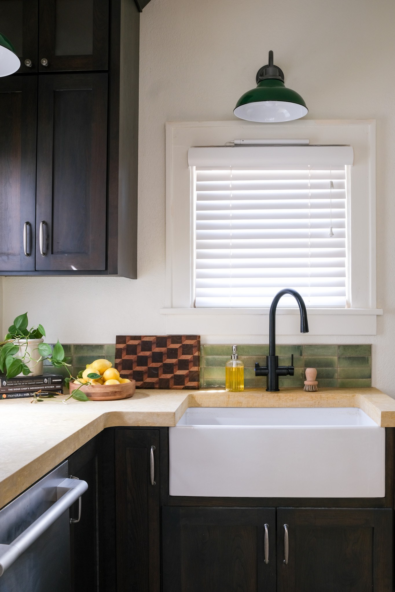 A white apron farmhouse sink with limestone counter and green glazed tile