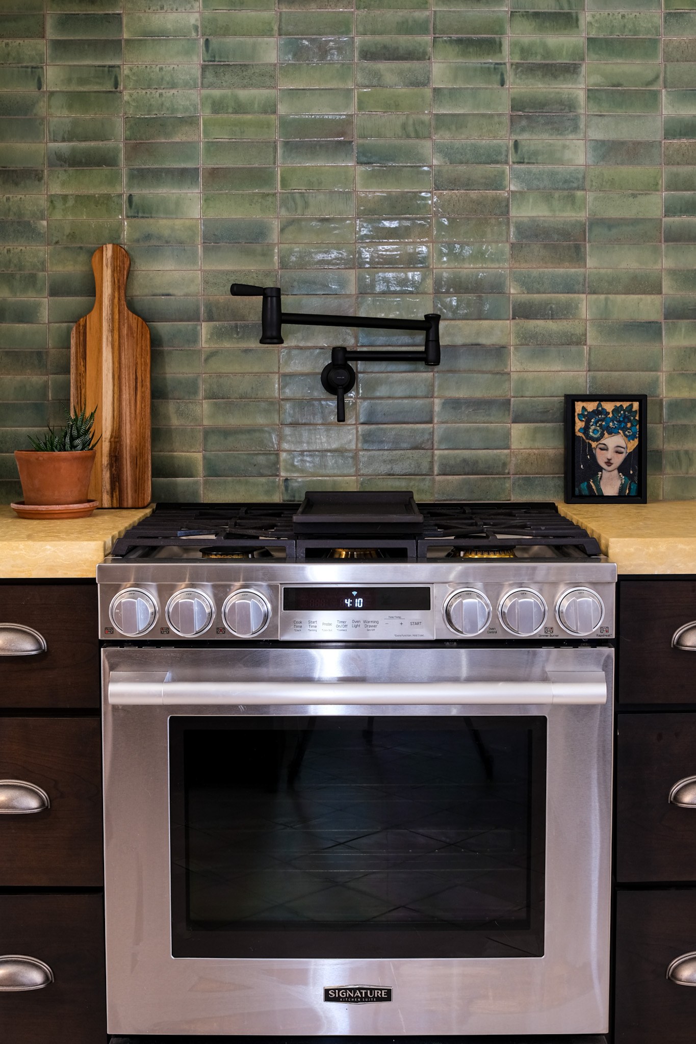 A stainless gas range with a matte black pot filler on a green glazed tile range wall